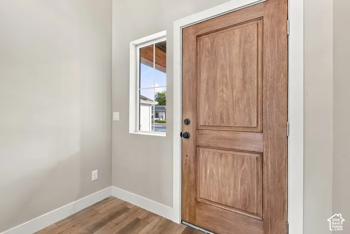 Solid wood-finish door with recessed panels, dark hardware, and multi-pane window with white trim, complemented by wood-finish flooring