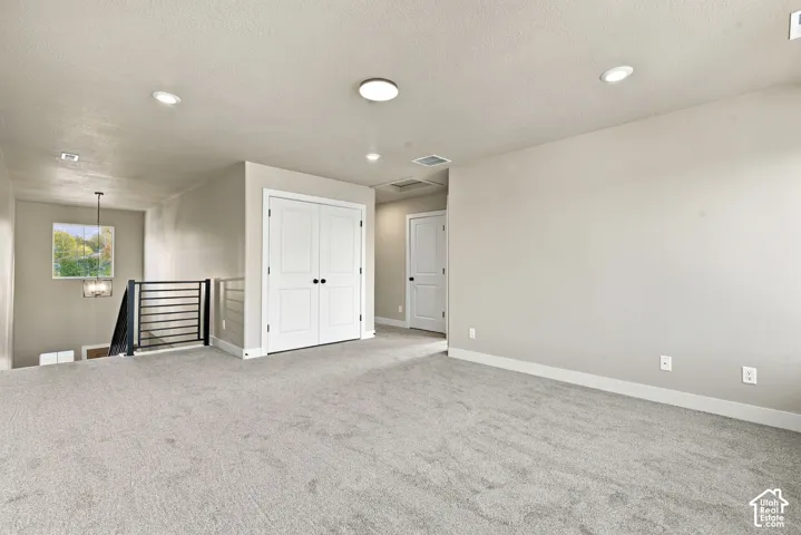 Neutral-toned interior space featuring recessed ceiling lighting, wall-to-wall carpeting, metal stair railing, and dual-panel closet doors
