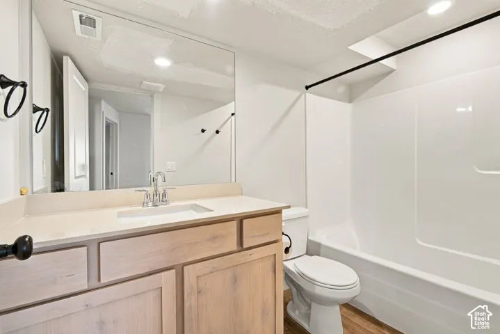 Full bathroom featuring a light-toned wood-finish vanity with a solid-surface integrated sink, a large wall-mounted mirror, and a tub-shower combination with a white surround