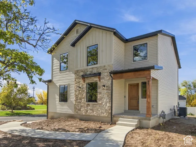 Two-story exterior featuring a mix of horizontal siding and vertical board-and-batten siding, natural stone facade, covered entryway with a timber-finished pillar, and a concrete walkway