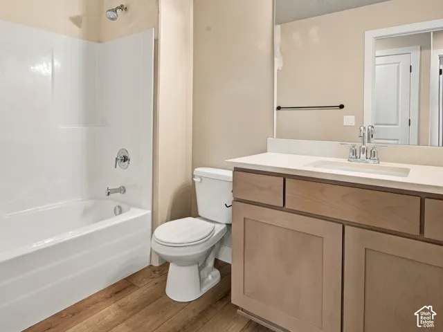 Bathroom featuring a light wood-finish vanity, solid-surface countertop with an integrated sink, wood-finish flooring, white tub-shower combination, and a multi-light fixture