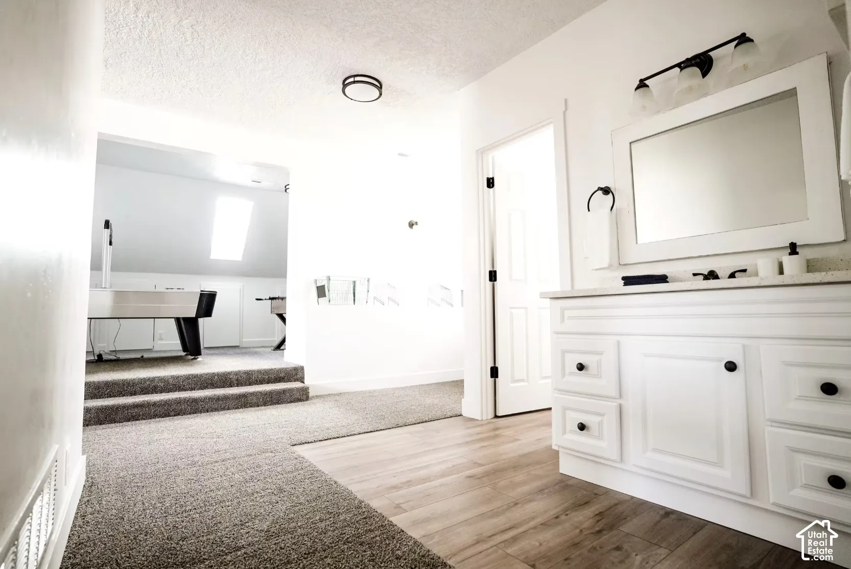 White built-in vanity with shaker-style cabinetry, neutral stone-finish countertop, dual-light vanity fixture, wall-mounted mirror, and wood-finish flooring