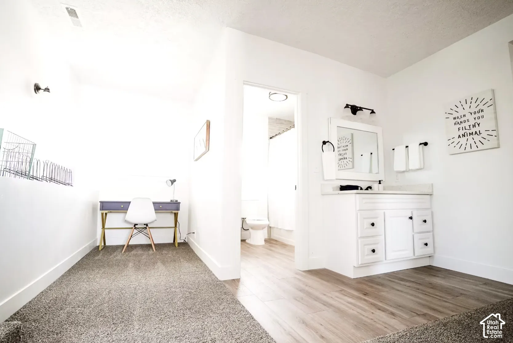 White vanity featuring a rectangular integrated sink, quartz-style countertop, and matte black hardware, accompanied by wood-finish flooring and a wall-mounted light fixture