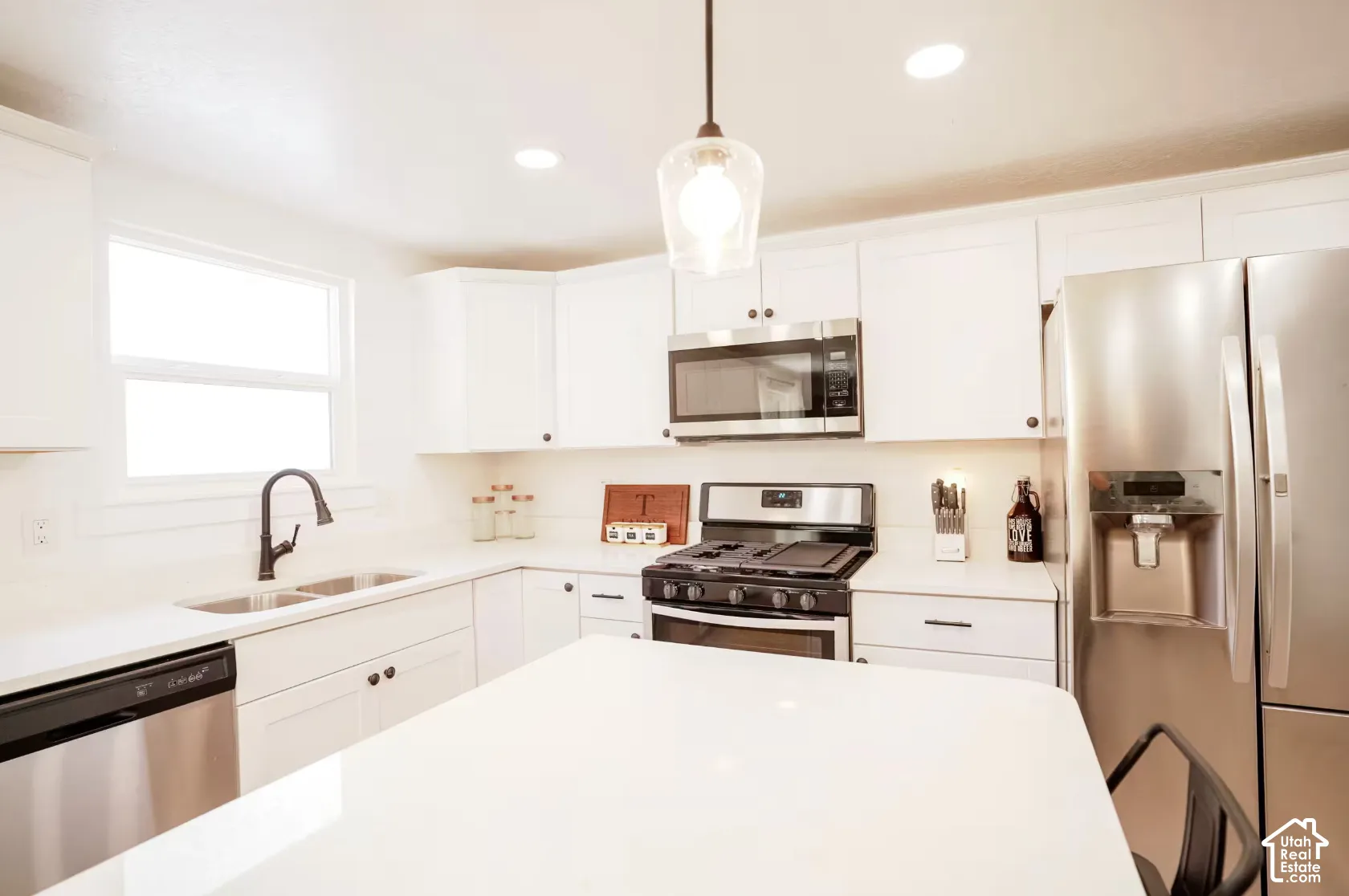 Kitchen featuring white shaker-style cabinetry, a central island with a solid surface countertop, stainless steel appliances, and a matte black gooseneck faucet