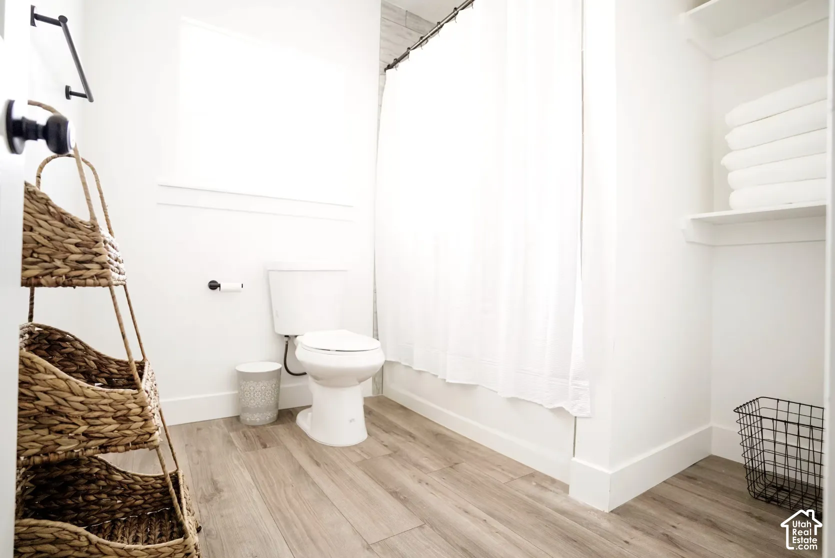 Bathroom featuring wood-finish flooring, a matte black towel bar, a white porcelain toilet, and built-in shelving