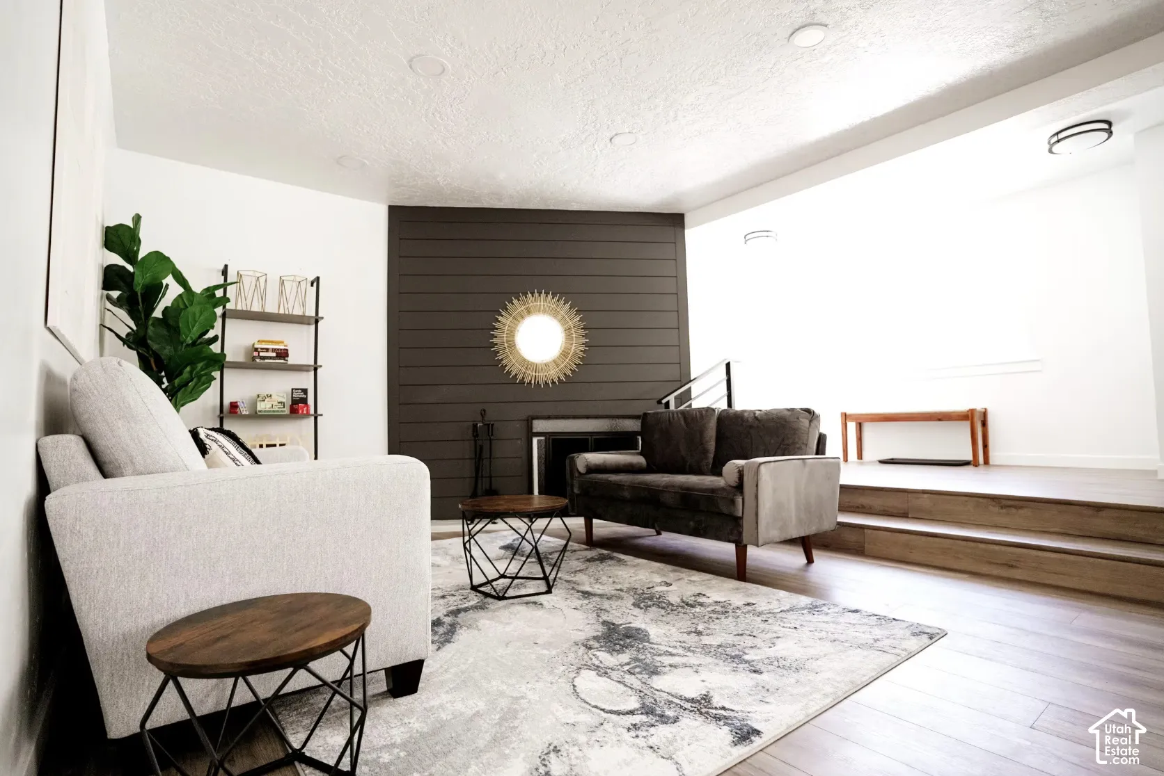 Living area featuring dark horizontal shiplap accent wall, fireplace with integrated metal surround, recessed ceiling lighting, and wood-finish flooring with a multi-level platform