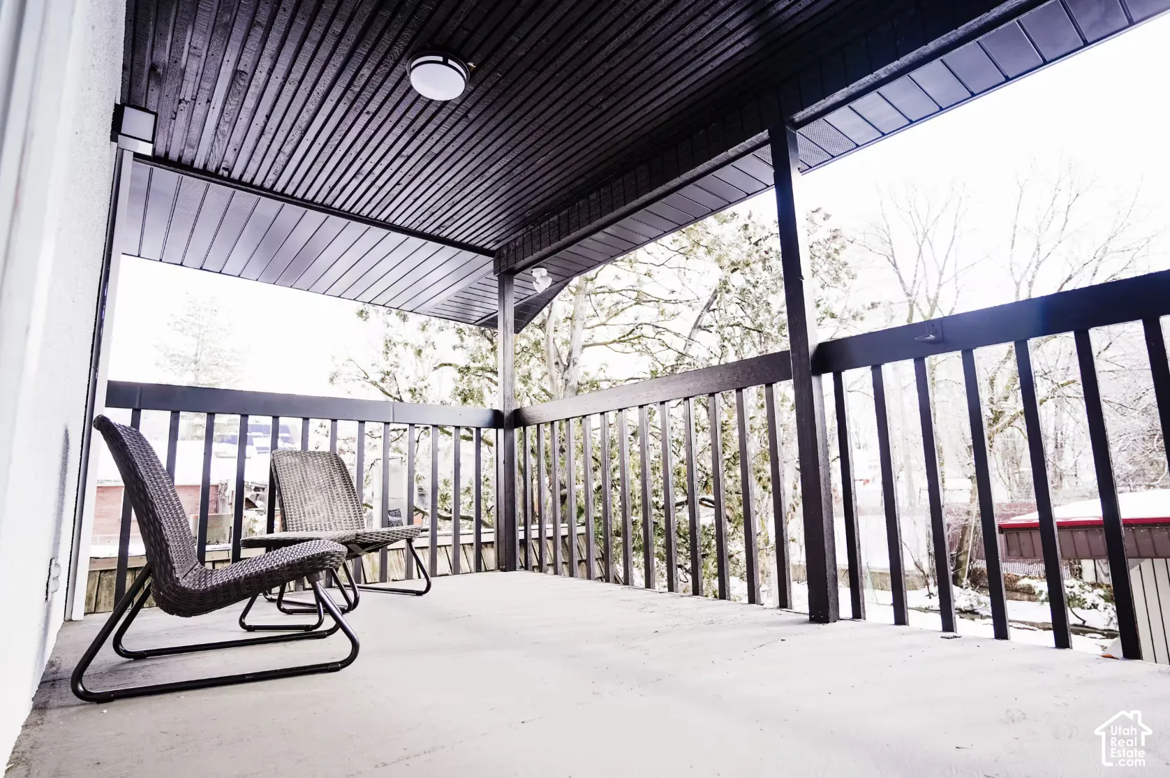 Covered outdoor balcony featuring dark-finished tongue-and-groove ceiling paneling, a matching wooden railing, and an integrated ceiling light fixture