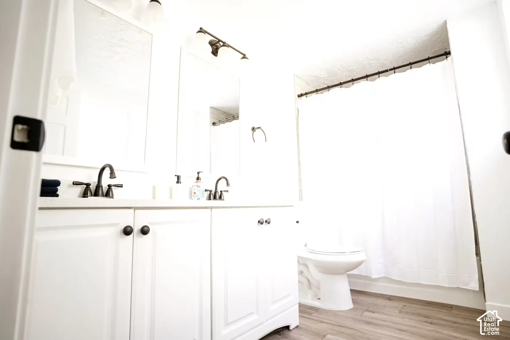 Bathroom featuring a white double-sink vanity with stone-style countertop, dark finish hardware, dual wall-mounted mirrors, and wood-finish flooring
