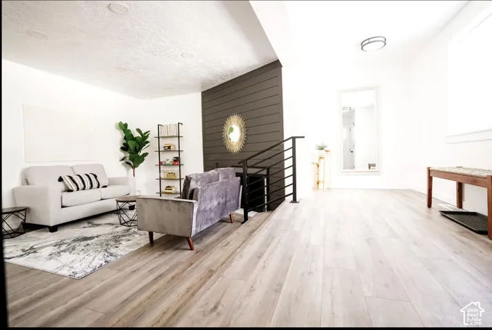 Light-toned wood-finish flooring, dark shiplap accent wall, recessed ceiling lighting, and metal horizontal-bar stair railing
