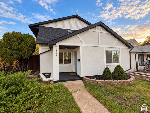 Exterior featuring light-toned stucco siding with dark timber-style accents, a front porch with a covered entryway, and curved stone-block landscaping borders