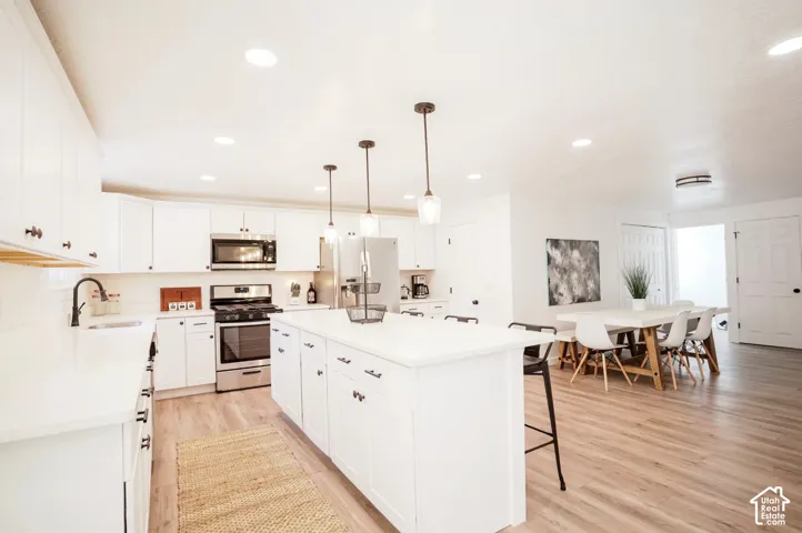 Kitchen featuring white shaker-style cabinetry, quartz countertops, stainless steel appliances, a center island with pendant lighting, and wood-finish flooring