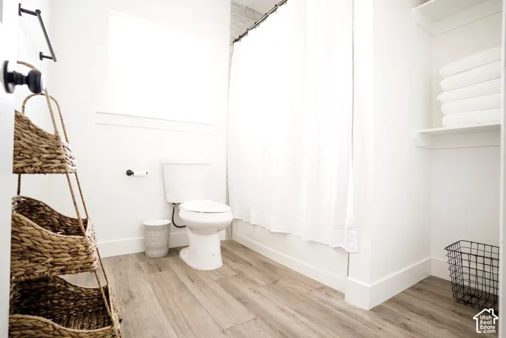 Bathroom featuring wood-finish flooring, a matte black towel bar, a white porcelain toilet, and built-in shelving