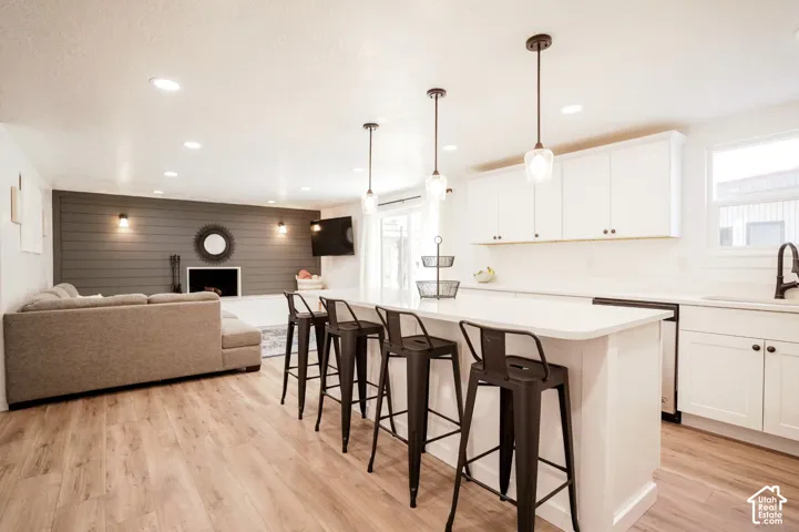 Kitchen featuring white cabinetry, an expansive island with quartz countertops, wood-finish flooring, recessed lighting, and three glass pendant lights, complemented by a charcoal shiplap accent wall with a fireplace