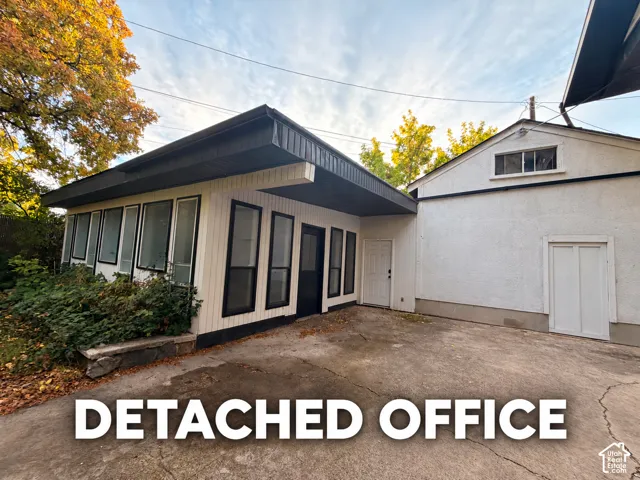 Detached structure featuring vertical wood siding, extensive glazing, a prominent roof overhang, and concrete hardscaping
