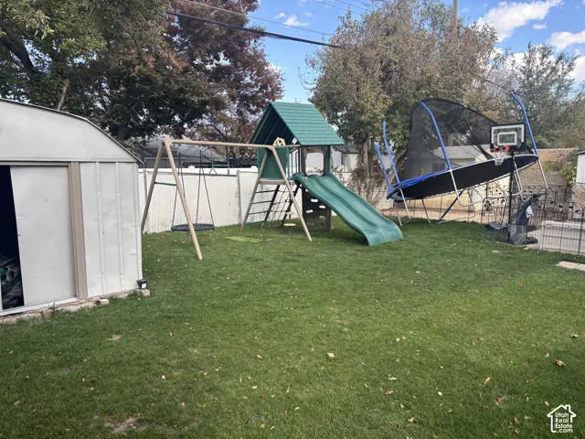 Fenced backyard featuring a manicured lawn, perimeter white vinyl fencing, and a detached metal storage shed