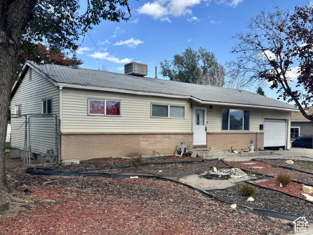 Single-story exterior featuring light-toned vinyl siding, lower-level brick masonry, an attached garage, and a roof-mounted cooling unit