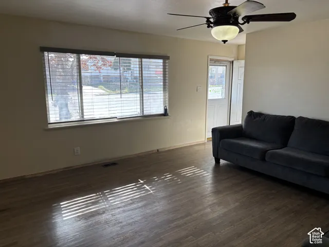 Wood-finish flooring, large window with horizontal blinds, and ceiling fan with integrated lighting