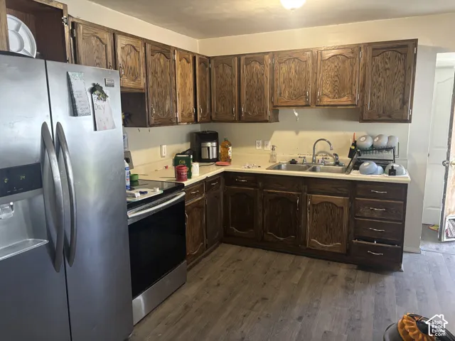 Kitchen featuring wood cabinetry, stainless steel side-by-side refrigerator, integrated stovetop, dual-basin sink with pull-down faucet, and wood-finish flooring