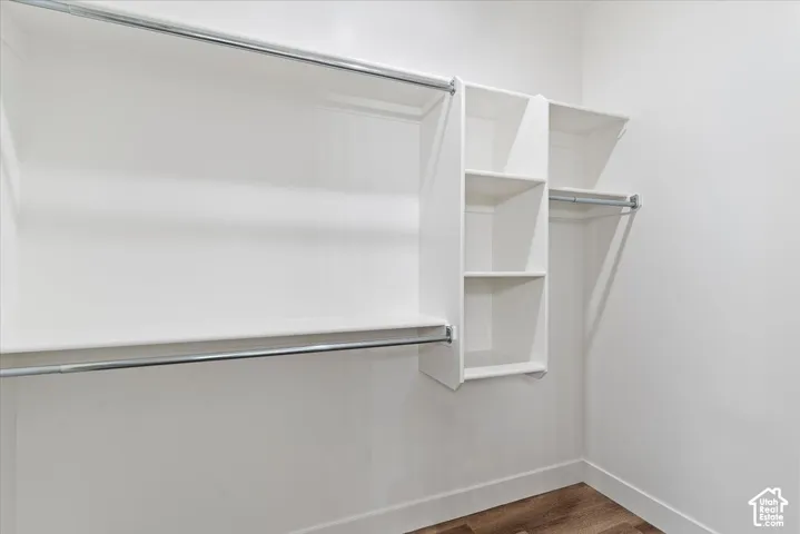 Walk-in closet featuring white built-in shelving, multi-level metal garment rods, and wood-finish flooring