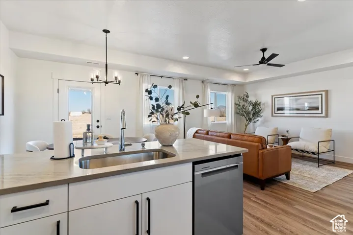Kitchen island featuring quartz countertops and an undermount stainless steel sink, complemented by flat-panel cabinetry with matte black hardware, stainless steel dishwasher, wood-finish flooring, and recessed ceiling lighting