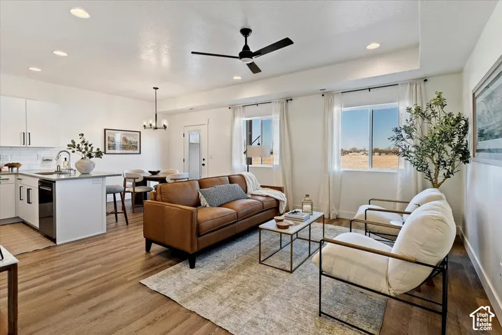 Open-concept living space featuring wood-finish flooring, recessed lighting, tray ceiling, kitchen island with built-in cabinetry, and black matte ceiling fan