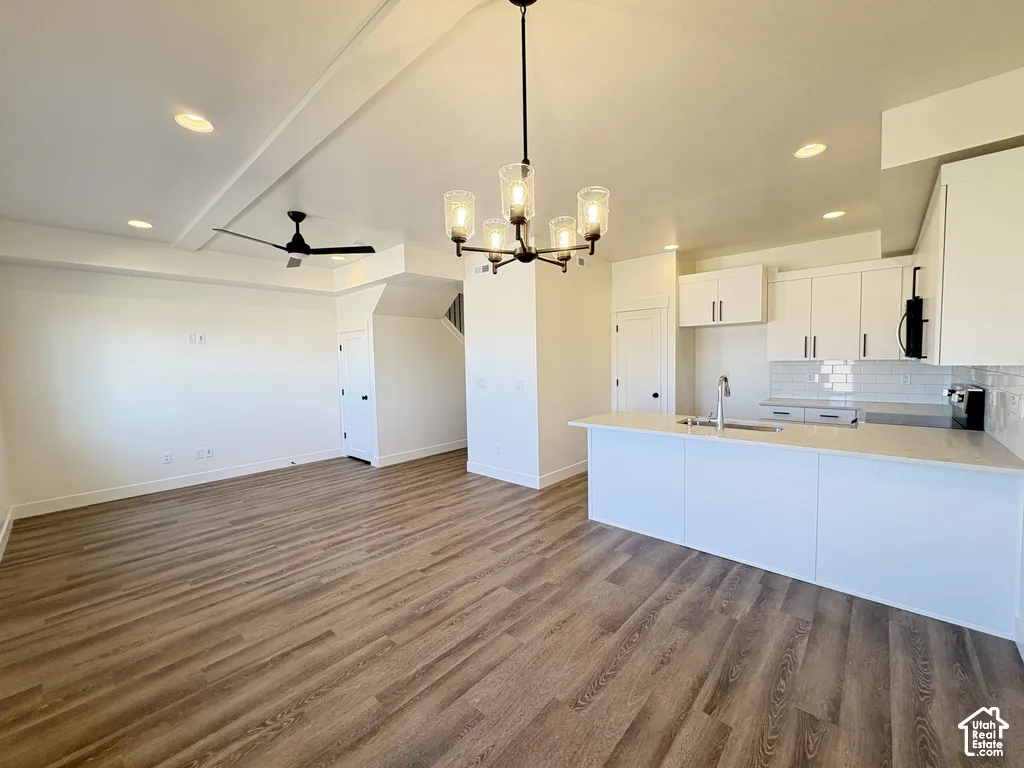 Open-concept interior featuring wood-finish flooring, white cabinetry, quartz countertops, a subway tile backsplash, and a six-light chandelier