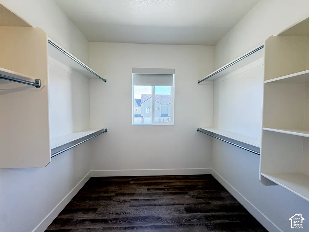 Walk-in storage space featuring wood-finish flooring, white built-in shelving, metal garment rods, and a single window