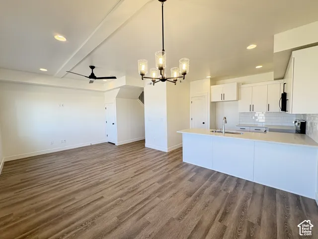 Open-concept interior featuring wood-finish flooring, white cabinetry, quartz countertops, a subway tile backsplash, and a six-light chandelier