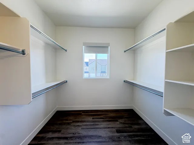 Walk-in storage space featuring wood-finish flooring, white built-in shelving, metal garment rods, and a single window