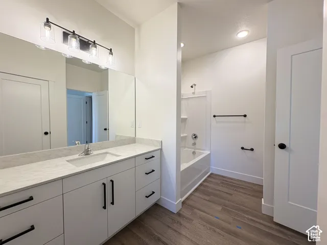 Bathroom featuring a white vanity with stone-finish countertop, undermount sink, matte black hardware, integrated tub and shower unit, and wood-finish flooring