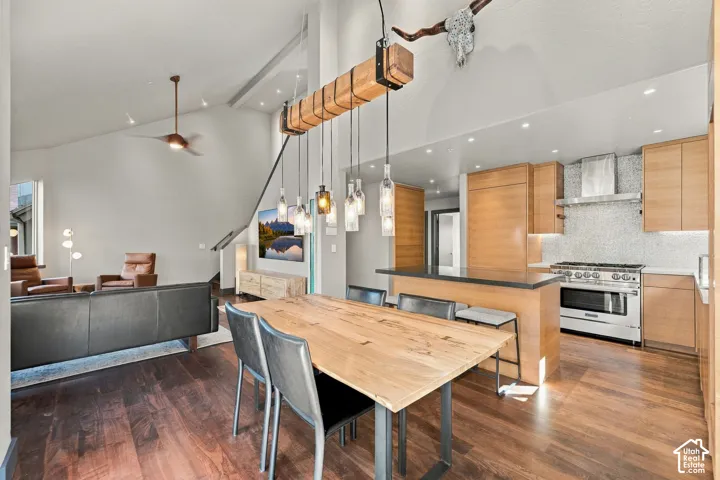 Open-concept living space featuring vaulted ceilings, wood-finish flooring, a kitchen with flat-panel cabinetry and a mosaic-tile backsplash, and a custom timber-beam pendant light fixture