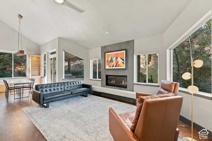 Vaulted ceilings, linear fireplace with floor-to-ceiling stone-finish surround, wood-finish flooring, multi-pane picture windows, and built-in glass-shelved cabinetry