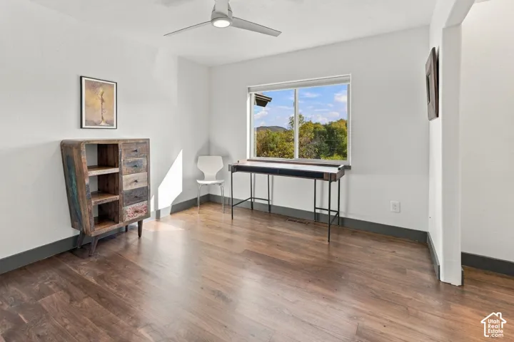 Room featuring wood-finish flooring, dark-toned trim, a sliding window with exterior greenery, and a ceiling-mounted light fixture