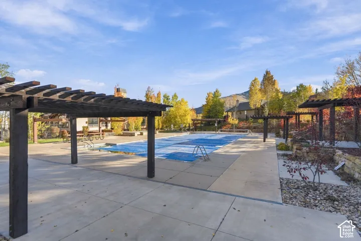 Outdoor swimming pool featuring expansive concrete decking, multiple wooden pergolas, and stone retaining walls