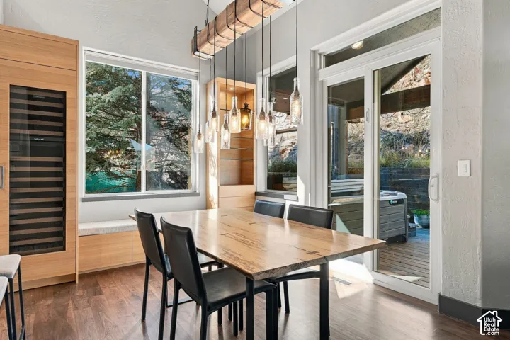 Dining area featuring wood-finish flooring, a linear timber-beam light fixture with glass pendants, custom floor-to-ceiling wood cabinetry, a built-in wine refrigerator, and glass sliding doors