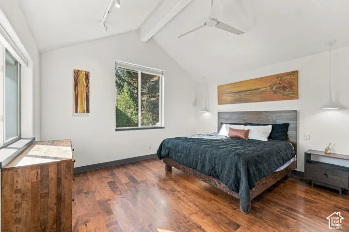 Vaulted ceilings with exposed structural beam, wood-finish flooring, dual modern pendant lighting, and track lighting