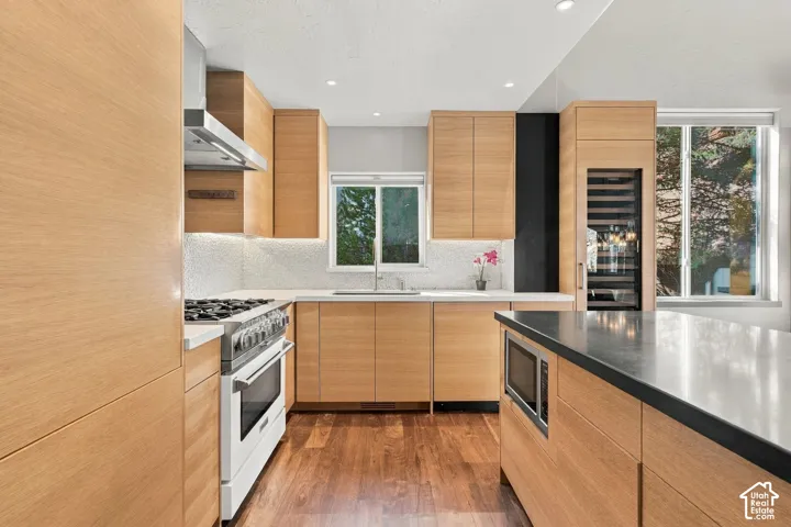 Kitchen featuring flat-panel wood cabinetry, integrated wine refrigerator, stainless steel gas range with overhead vent hood, and solid surface countertops