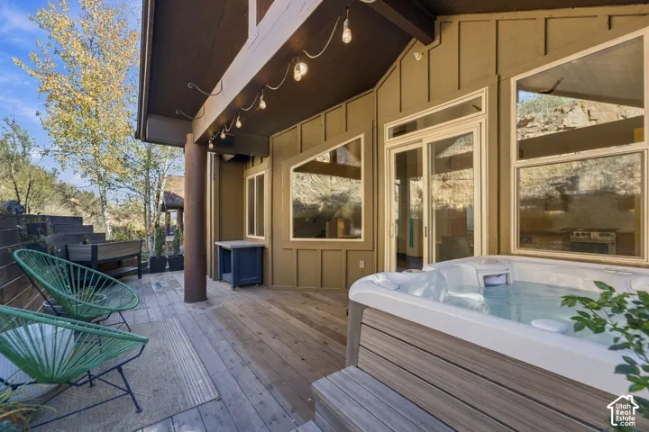 Covered exterior patio featuring wood decking, a built-in hot tub, vertical board-and-batten siding, and oversized custom-shaped windows