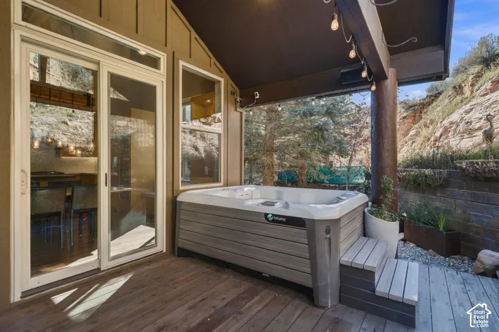 Covered outdoor deck featuring wood-finish decking, built-in hot tub with integrated steps, glass sliding door, and rock formation backdrop