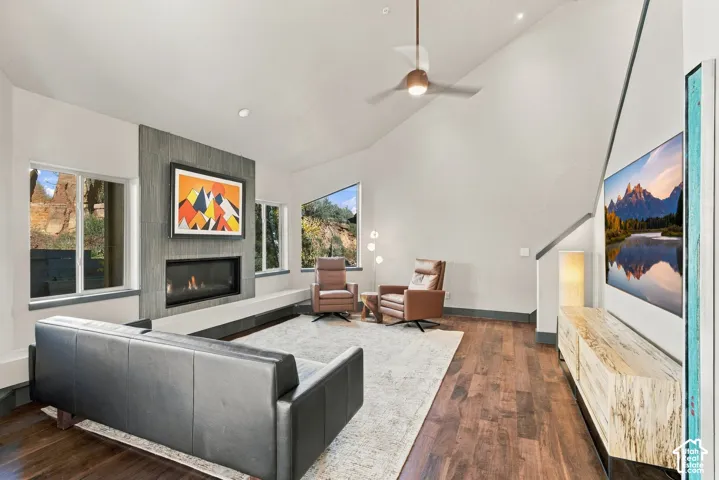 Vaulted ceilings, wood-finish flooring, linear fireplace with textured surround, and expansive windows