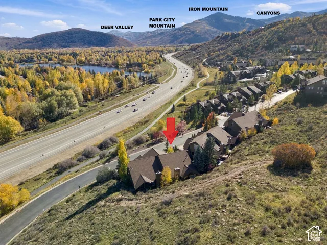 Aerial perspective featuring a multi-unit residential structure with dark shingle roofing, brick chimney stacks, and natural mountain terrain