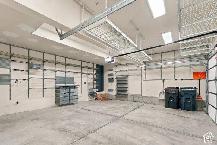 Multi-car garage featuring extensive wall-mounted shelving systems, overhead wire storage racks, concrete flooring, and recessed ceiling lighting