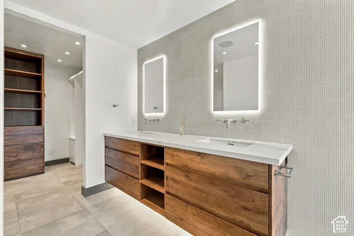 Floating vanity with wood-finish cabinetry, dual undermount sinks, stone-surface countertop, LED-backlit mirrors, and wall-mounted faucets