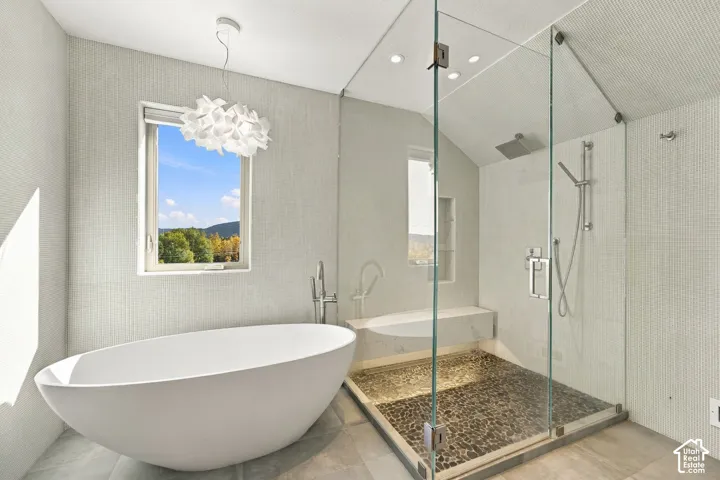 Freestanding soaking tub with floor-mounted faucet, glass-enclosed shower featuring a river-rock floor, built-in stone shower bench, and textured wall surfaces
