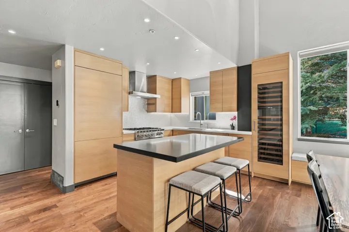 Kitchen featuring flat-panel wood cabinetry, integrated stainless steel appliances, a center island with a dark solid-surface countertop, built-in wine storage, and wood-finish flooring