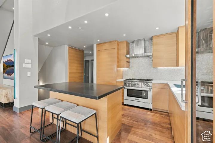 Kitchen featuring wood-finish cabinetry, a central island with a dark solid-surface countertop, stainless steel professional-grade range, tiled backsplash, and wood-finish flooring