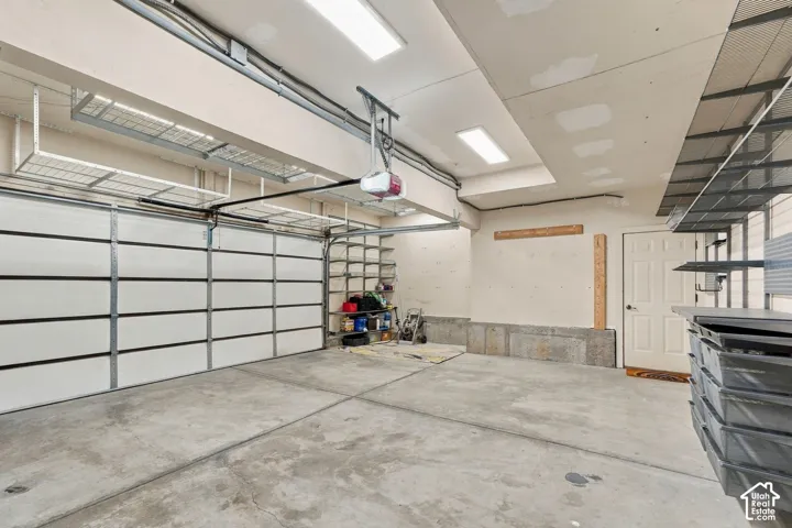 Garage featuring expansive overhead metal shelving, built-in wall-mounted storage racks, concrete flooring, and ceiling-mounted linear lighting fixtures