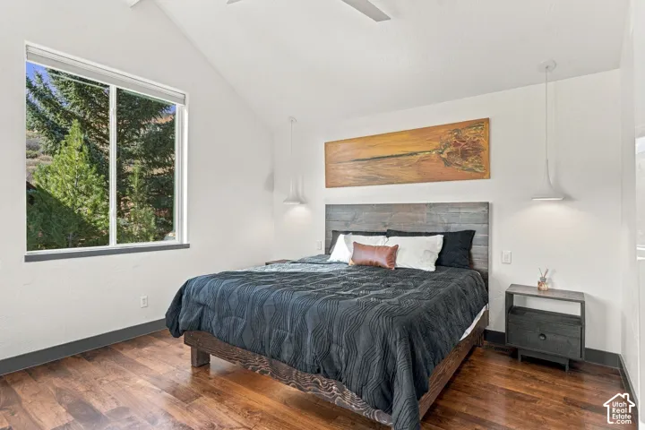 Vaulted ceiling, wood-finish flooring, dual minimalist pendant lights, and large window with exterior tree scenery