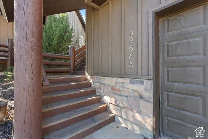 Exterior entrance featuring vertical board-and-batten siding, stone masonry base, wood-finish stairs, and a log-style structural post