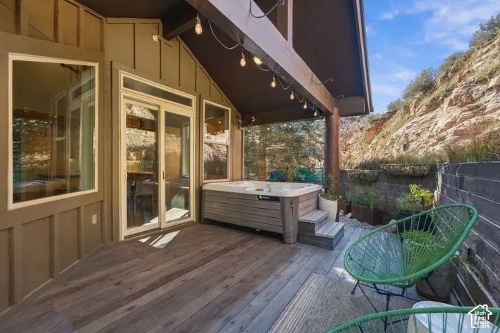 Covered wood deck featuring a built-in spa, board-and-batten siding, large sliding glass doors, and expansive rock formation backdrop